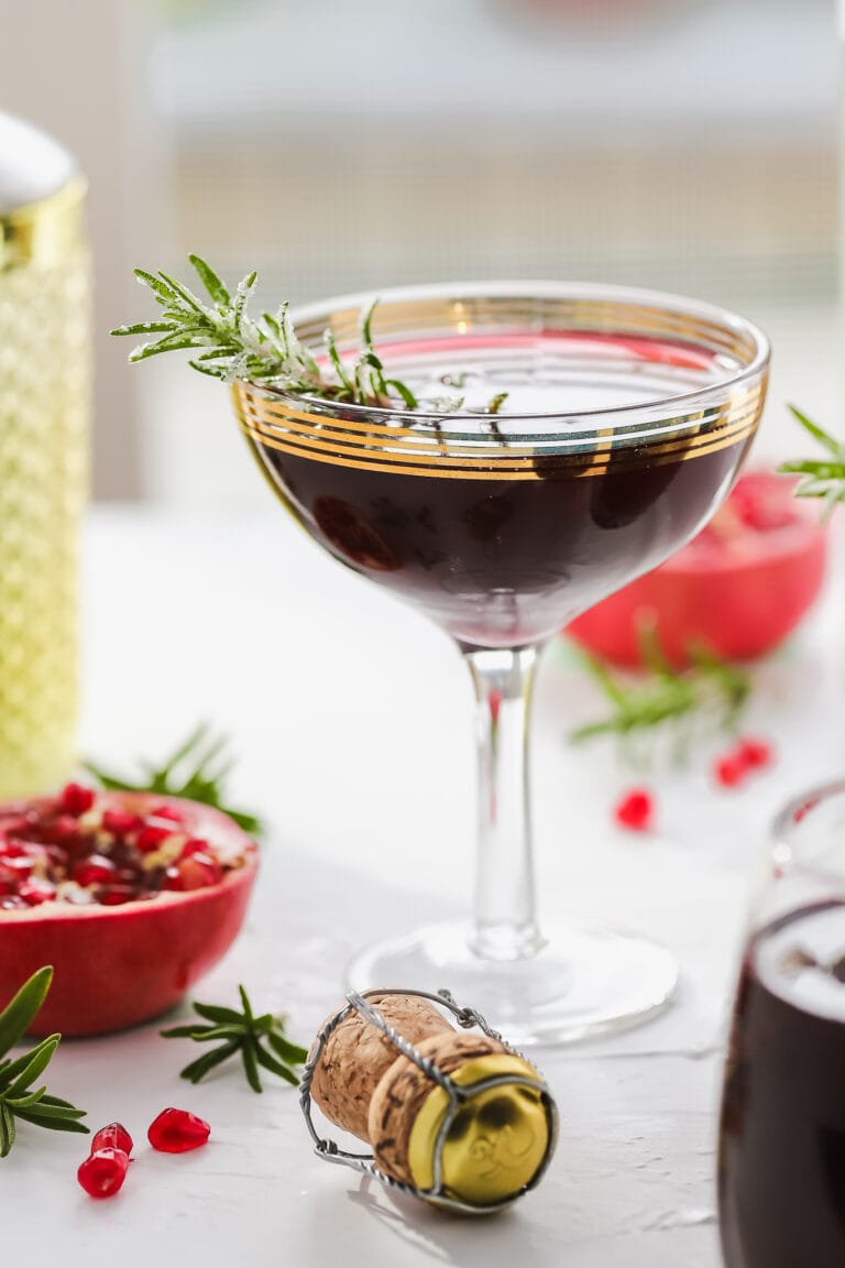 pomegranate cocktail in a coupe glass garnished with rosemary sprig