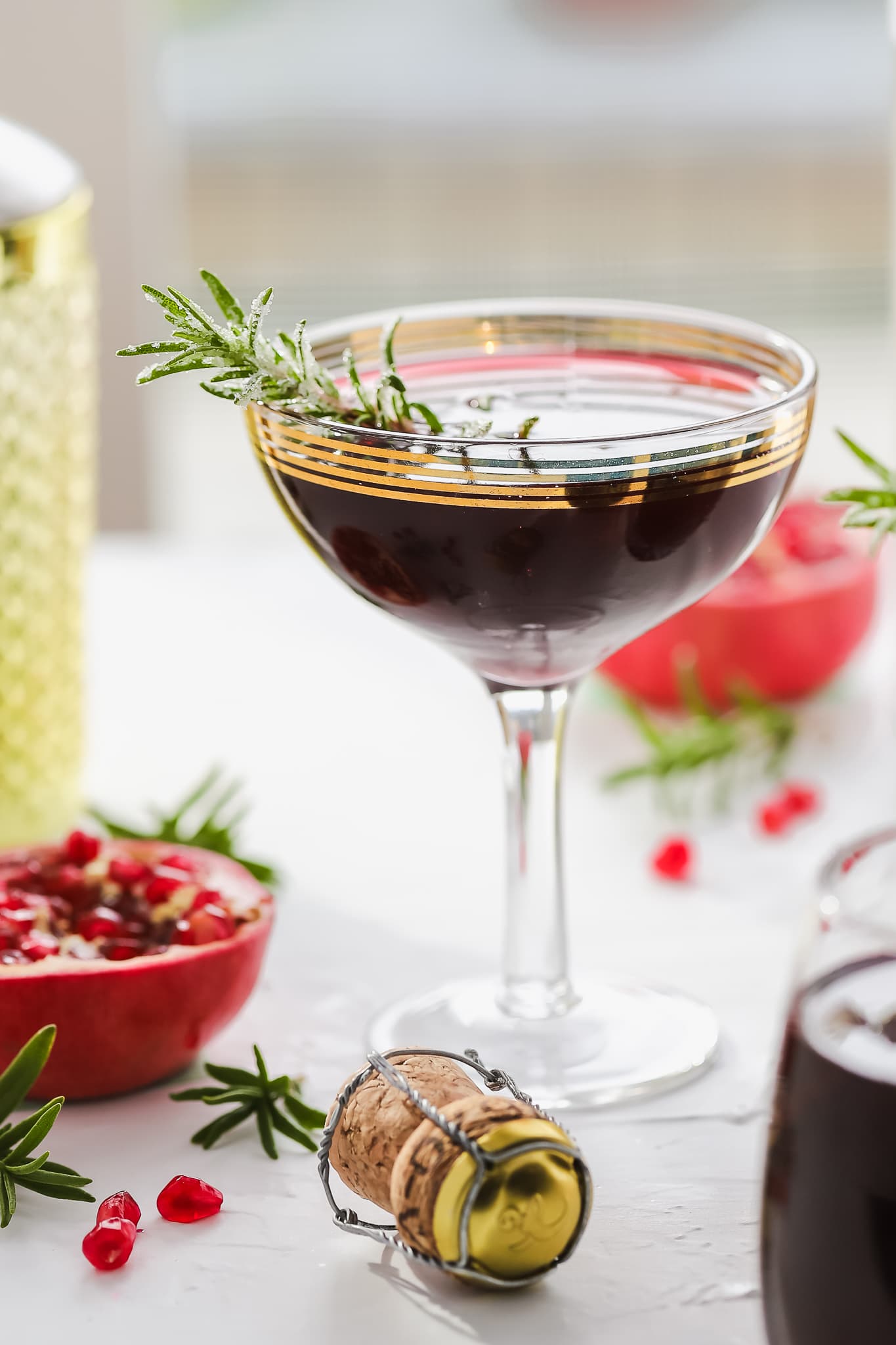 pomegranate cocktail in a coupe glass garnished with rosemary sprig