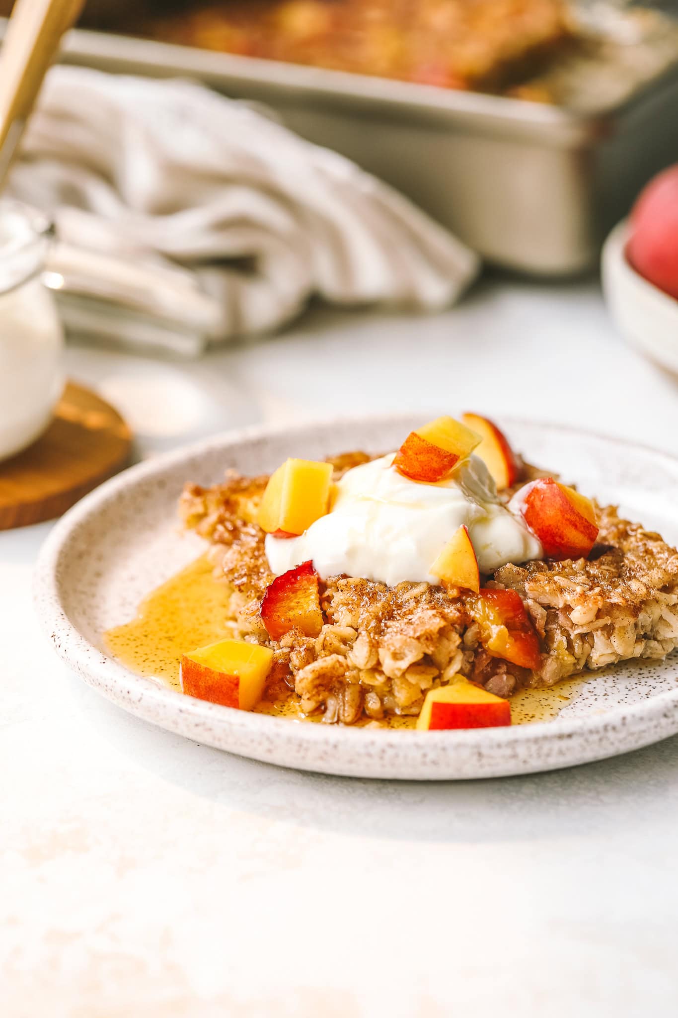 angled shot of peach baked oatmeal on a plate with yogurt and peaches