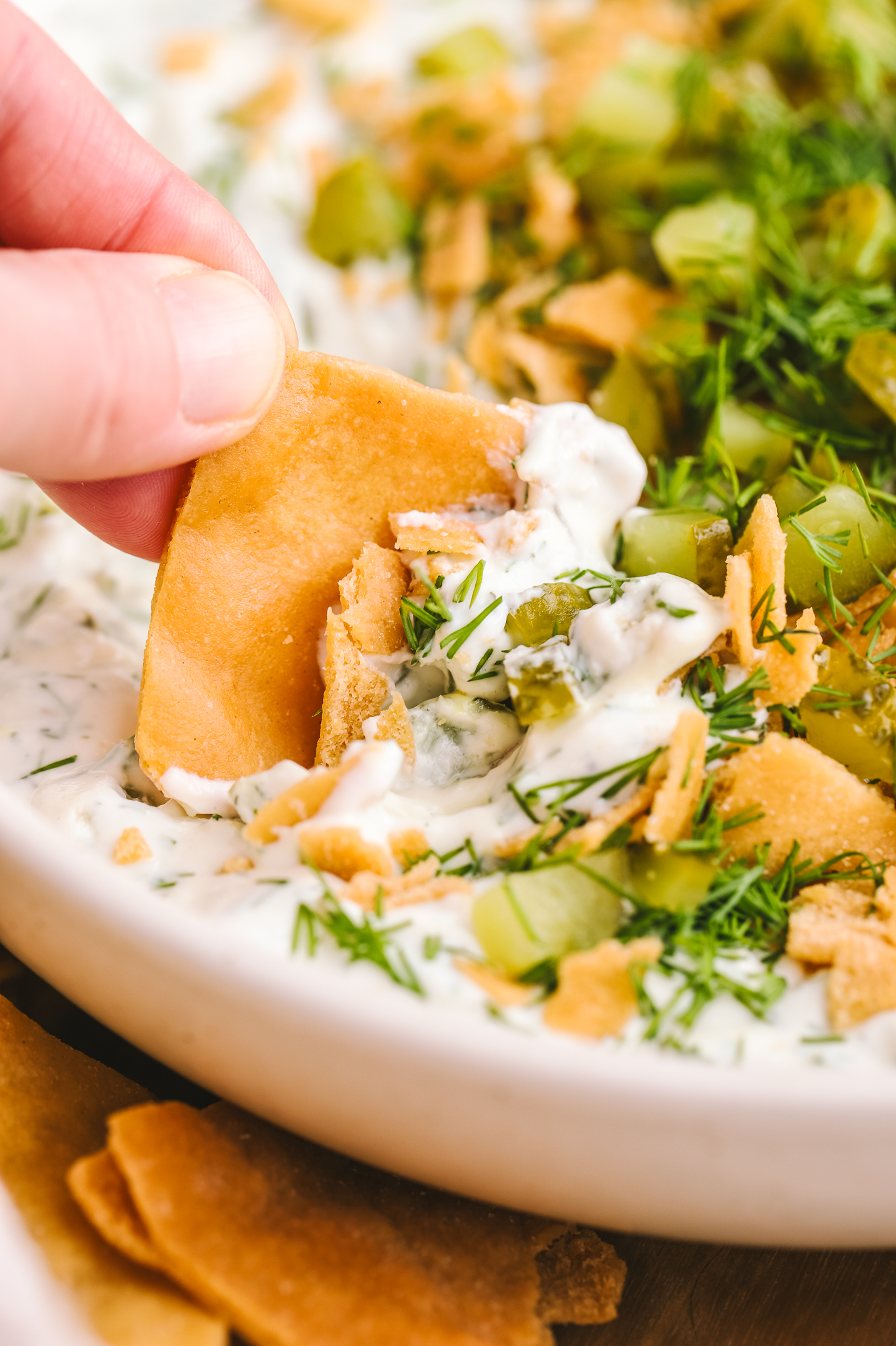 hand dipping pita chip into dill pickle dip