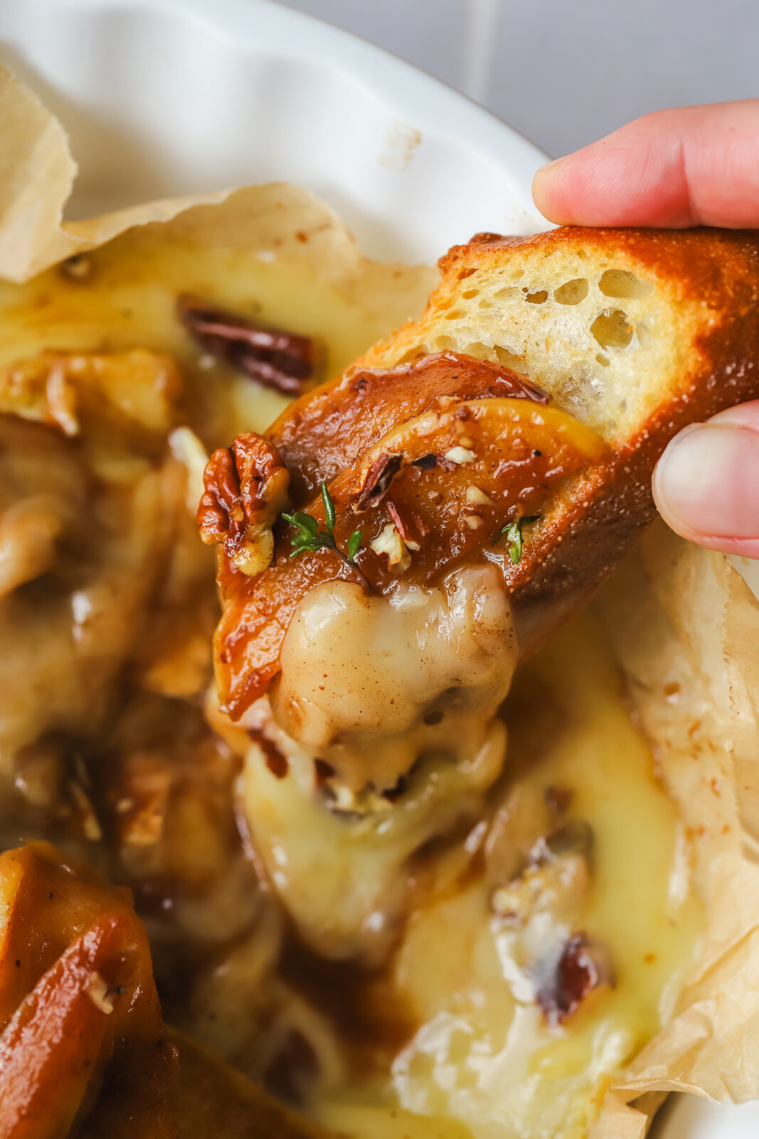 hand holding crostini dipping into baked brie