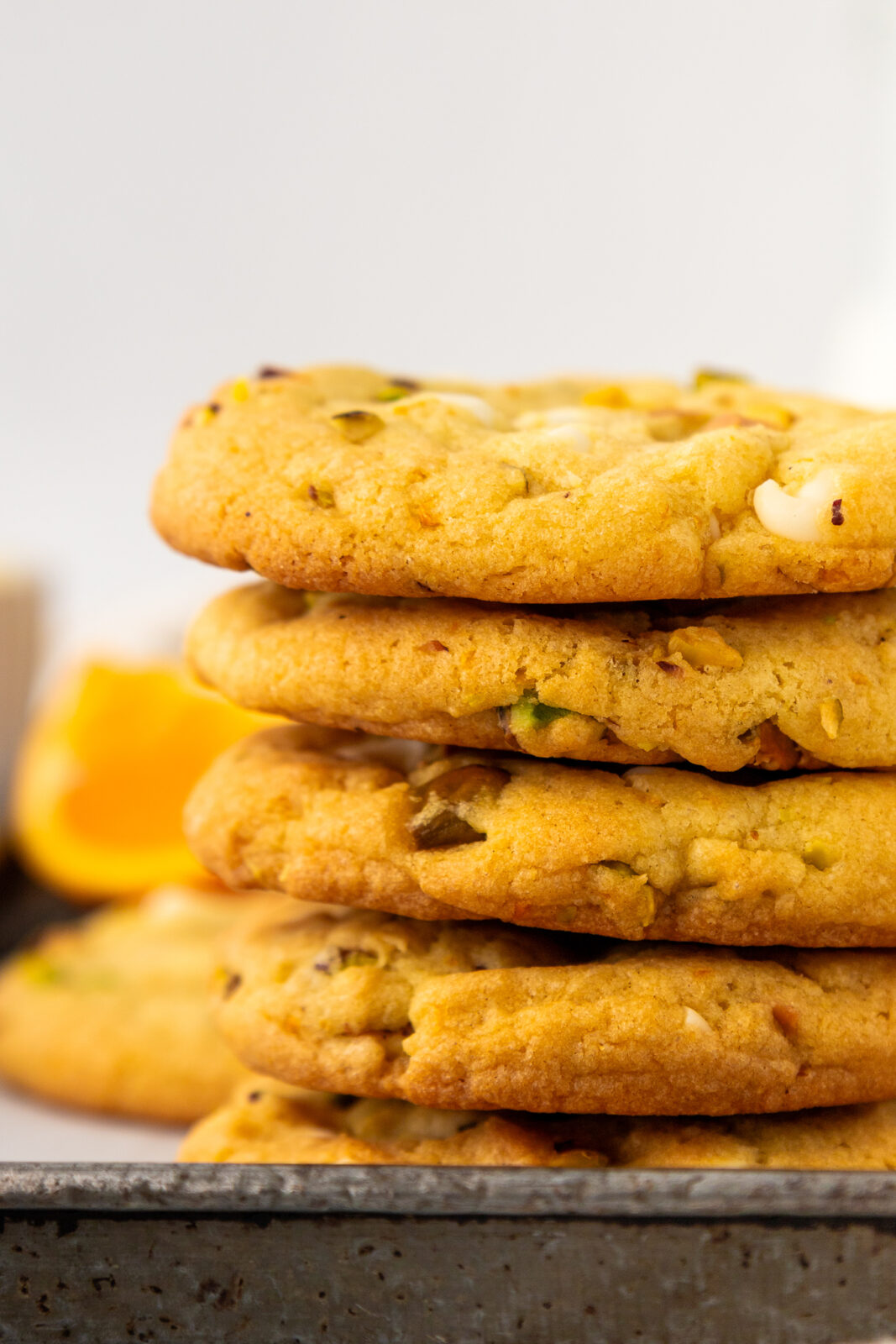 close up of a stack of orange pistachio white chocolate cookies