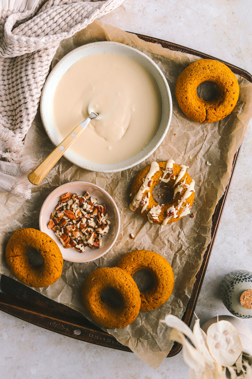 maple icing in a bowl, pecans in a bowl and pumpkin donuts