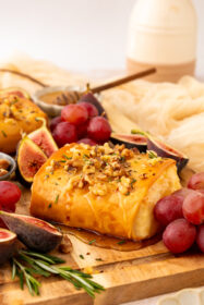 side angle of baked feta on a serving board with grapes and figs