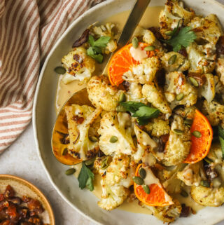 roasted cauliflower in a serving dish with orange tahini sauce